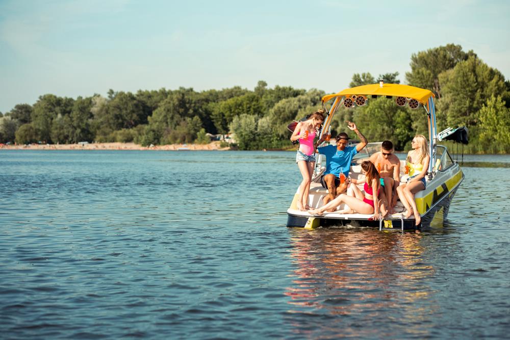 Company of friends sitting on the deck of a pontoon boat while holding bottles of drinks in their hands